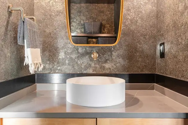 Homewood bathroom addition with round vessel sink, textured metallic wall finish and brass framed mirror