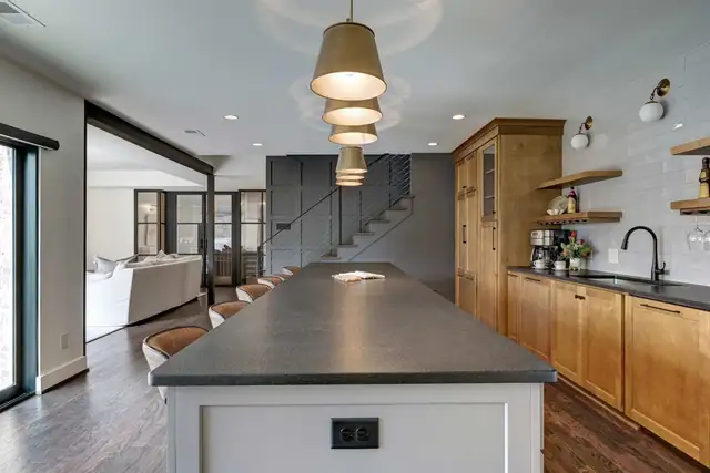 Vestavia Hills basement renovation with long dark-topped island, natural wood cabinets, open shelving and brass pendant lights