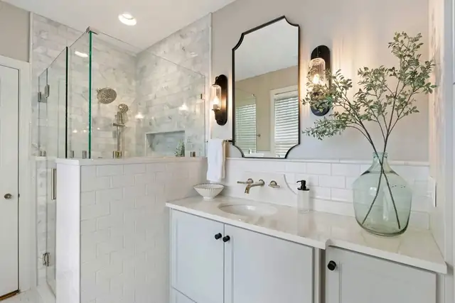 Homewood bathroom renovation with frameless glass shower in marble tile, white vanity, scalloped black mirror and brass sconces