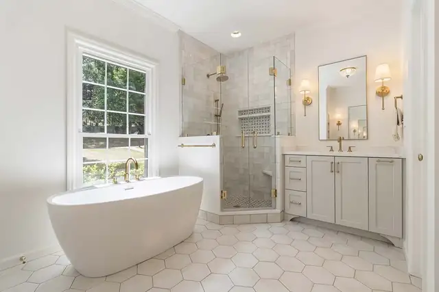Homewood primary bath with freestanding tub, white hexagon floor tile, corner glass shower and brass fixtures