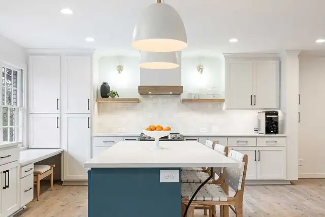 Vestavia kitchen with white cabinets, blue island with seating, white dome pendants and a built-in desk nook