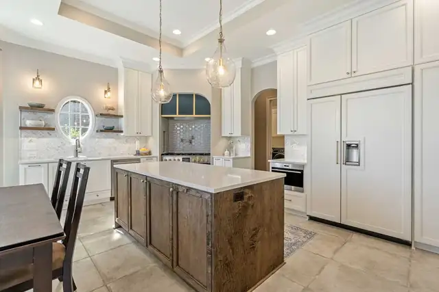 Kitchen renovation with a stained wood island, cream cabinetry, a paneled refrigerator and glass pendant lights