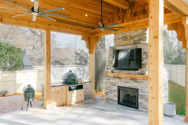 Hoover covered porch with cedar ceiling, stacked stone fireplace with mounted TV, ceiling fans and an outdoor grill station