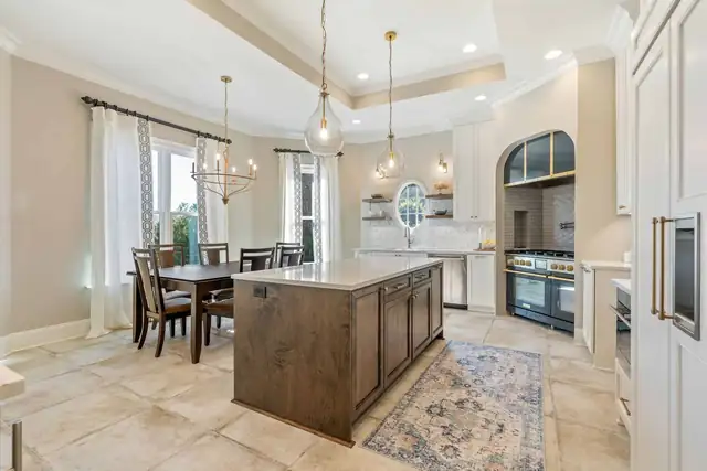 Kitchen by ELM Construction with a stained wood island, white perimeter cabinets, glass pendants and an arched range alcove